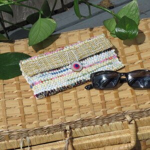 Boho Wallet Smart Phone Case, Small Hand Woven Clutch Purse, Cloth Fabric Soft Eyeglass Case Handmade Vegan Eco Friendly Zero Waste Upcycled Recycled Bag, Sustainable Slow Fashion Accessory with Sunny Yellow Accents Handcrafted by Amy C. Lund! Showing button closure. Styled with sunglasses on a basket with green leaves.
