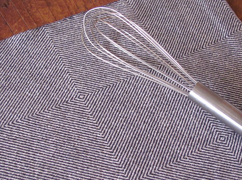 A Navy Blue and White Hand Woven Twill Block Pattern kitchen towel, shown as an example for Table or Floor Loom Weaving Pattern Draft PDF, 4 H Harness Shaft Handweaving Cotton Kitchen Hand Woven Dish Tea Towel Downloadable Tutorial, an artful Kitchenware, Cookware Accessory for Gourmet Chef, Home Baking, Cooking, Instructions Designed by Master Weaver Amy C. Lund. Pictured with a silver metal whisk with a handle.