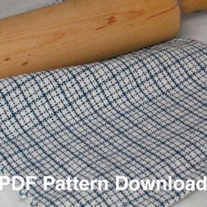 May include: A white kitchen towel with a blue and white checkered pattern. The towel is folded and a wooden rolling pin is lying on top of it. The text "PDF Pattern Download" is printed on the towel.