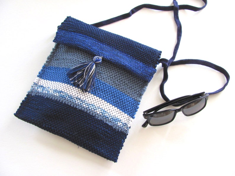 Small Crossbody Bag Wallet or Phone Purse is Handmade, Artisan Hand Woven in Indigo Navy Blue with Zero Waste, Eco Friendly Upcycled Cloth, Vegan Recycled Fabric. This Sustainable Slow Fashion Accessory Handbag, Boho Cash Change Pouch or Money Shoulder Pouch is Handcrafted by Amy C. Lund. Styled casually with black sunglasses.