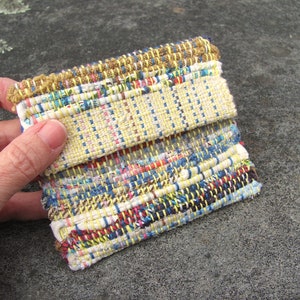 May include: A woven fabric coaster with a yellow, blue, red, and white pattern. The coaster is made of recycled materials and has a rustic, handmade look.