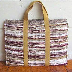 May include: A woven tote bag with brown, white, and burgundy stripes. The bag has two wide, tan straps.