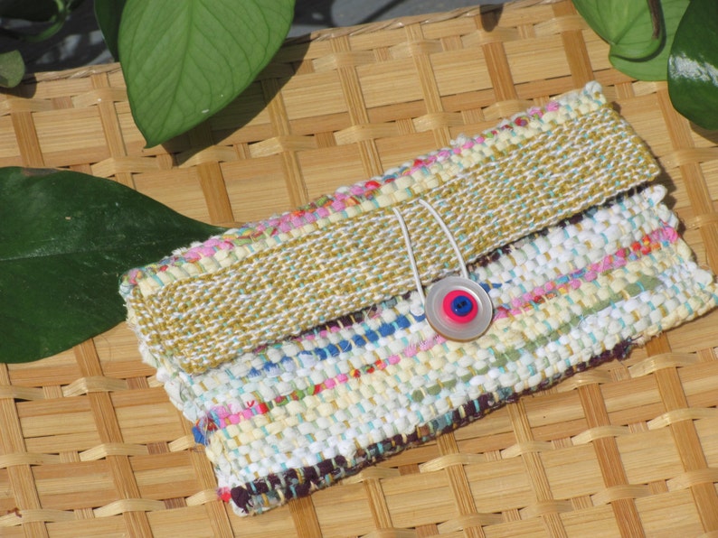 Boho Wallet Smart Phone Case, Small Hand Woven Clutch Purse, Cloth Fabric Soft Eyeglass Case Handmade Vegan Eco Friendly Zero Waste Upcycled Recycled Bag, Sustainable Slow Fashion Accessory with Sunny Yellow Accents Handcrafted by Amy C. Lund! Showing button closure. Styled on a basket with green leaves.