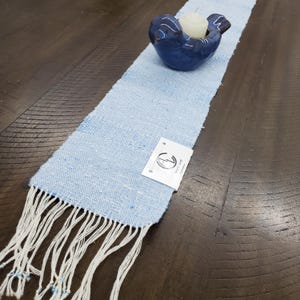 Artisan Handmade Light Blue Spring Summer Scarf, Minimalist Zen Serenity, Simplicity, Soothing Tranquil Tones Meditation Table Runner, Gender Neutral Unisex Men's or Women's Om Yoga, Spiritual Prayer Clothing, Hand Woven Cotton Scarf, Slow Fashion Accessory or Home Decor Accent Gift Idea. Styled on a dark wood table with a blue ceramic dove holding a candle.