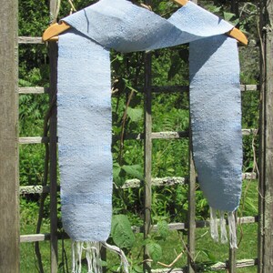 Artisan Handmade Light Blue Spring Summer Scarf, Minimalist Zen Serenity, Simplicity, Soothing Tranquil Tones Meditation Table Runner, Gender Neutral Unisex Men's or Women's Om Yoga, Spiritual Prayer Clothing, Hand Woven Cotton Scarf, Slow Fashion Accessory or Home Decor Accent Gift Idea. Styled casually on a hanger on a garden trellis.