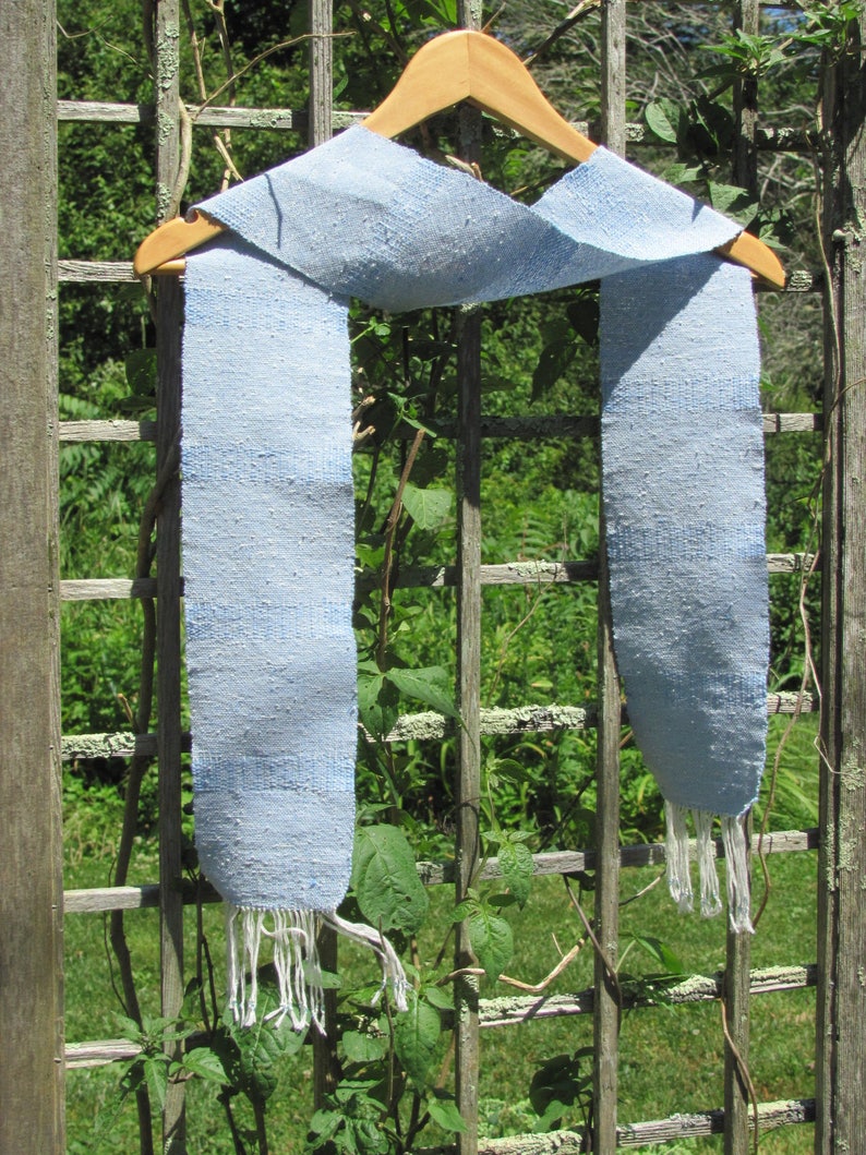 Artisan Handmade Light Blue Spring Summer Scarf, Minimalist Zen Serenity, Simplicity, Soothing Tranquil Tones Meditation Table Runner, Gender Neutral Unisex Men's or Women's Om Yoga, Spiritual Prayer Clothing, Hand Woven Cotton Scarf, Slow Fashion Accessory or Home Decor Accent Gift Idea. Styled casually on a hanger on a garden trellis.