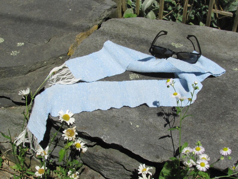 Artisan Handmade Light Blue Spring Summer Scarf, Minimalist Zen Serenity, Simplicity, Soothing Tranquil Tones Meditation Table Runner, Gender Neutral Unisex Men's or Women's Om Yoga, Spiritual Prayer Clothing, Hand Woven Cotton Scarf, Slow Fashion Accessory or Home Decor Accent Gift Idea. Styled casually on a gray rock with black sunglasses and white daisies.