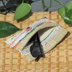 Boho Wallet Smart Phone Case, Small Hand Woven Clutch Purse, Cloth Fabric Soft Eyeglass Case Handmade Vegan Eco Friendly Zero Waste Upcycled Recycled Bag, Sustainable Slow Fashion Accessory with Sunny Yellow Accents Handcrafted by Amy C. Lund! Showing button closure. Styled on a basket with green leaves.