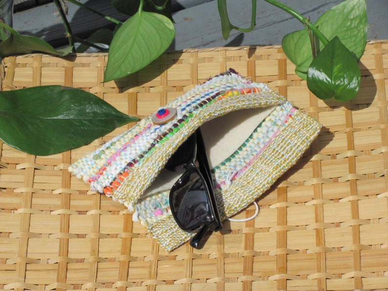 Boho Wallet Smart Phone Case, Small Hand Woven Clutch Purse, Cloth Fabric Soft Eyeglass Case Handmade Vegan Eco Friendly Zero Waste Upcycled Recycled Bag, Sustainable Slow Fashion Accessory with Sunny Yellow Accents Handcrafted by Amy C. Lund! Showing button closure. Styled on a basket with green leaves.
