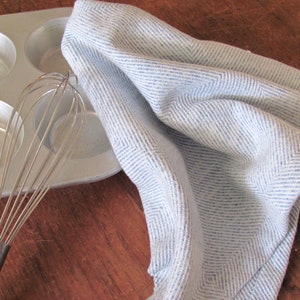 A blue and white Hand Woven Twill Block Pattern kitchen towel, shown as an example for Table or Floor Loom Weaving Pattern Draft PDF, 4 H Harness Shaft Handweaving Cotton Kitchen Hand Woven Dish Tea Towel Downloadable Tutorial, an artful Kitchenware, Cookware Accessory for Gourmet Chef, Home Baking, Cooking, Instructions Designed by Master Weaver Amy C. Lund. Pictured with silver metal muffin tin with a silver metal whisk.