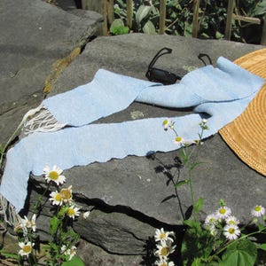Artisan Handmade Light Blue Spring Summer Scarf, Minimalist Zen Serenity, Simplicity, Soothing Tranquil Tones Meditation Table Runner, Gender Neutral Unisex Men's or Women's Om Yoga, Spiritual Prayer Clothing, Hand Woven Cotton Scarf, Slow Fashion Accessory or Home Decor Accent Gift Idea. Styled casually on a gray rock with black sunglasses and white daisies, a straw hat is in the background.