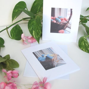 Two Spring Easter Egg Basket Greeting Cards, Blank Inside, Printable Instant Download PDF, Weaving Textile Art for Inspiration Hope Celebration. The cards are on a white surface with a green plant and pink flowers.