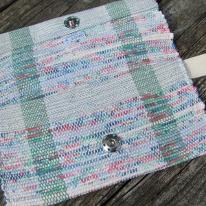 Upcycled Fabric Clutch Wallet, Boho Cloth Purse Pastel Wristlet Hand Bag, Handmade Hand Woven Zero Waste Sustainable Eco Vegan Recycled Accessories, Travel Jewelry Phone Pouch, Casual Spring or Summer Slow Fashion Accessory Handcrafted by Amy C. Lund in Pastel Pink, Green, Blue and Cream White with Button Accent. Styled open showing snap closure and wrist strap.