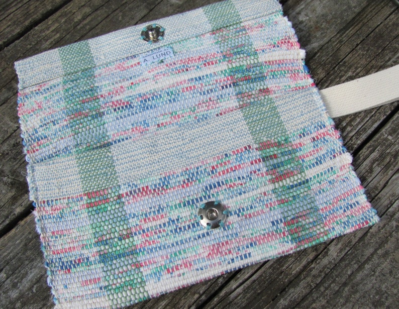 Upcycled Fabric Clutch Wallet, Boho Cloth Purse Pastel Wristlet Hand Bag, Handmade Hand Woven Zero Waste Sustainable Eco Vegan Recycled Accessories, Travel Jewelry Phone Pouch, Casual Spring or Summer Slow Fashion Accessory Handcrafted by Amy C. Lund in Pastel Pink, Green, Blue and Cream White with Button Accent. Styled open showing snap closure and wrist strap.