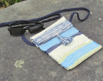 May include: A small, woven crossbody bag with a blue and white striped pattern. The bag has a tassel and a navy blue strap.