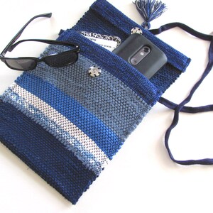 Small Crossbody Bag Wallet or Phone Purse is Handmade, Artisan Hand Woven in Indigo Navy Blue with Zero Waste, Eco Friendly Upcycled Cloth, Vegan Recycled Fabric. This Sustainable Slow Fashion Accessory Handbag, Boho Cash Change Pouch or Money Shoulder Pouch is Handcrafted by Amy C. Lund. Shown open with a phone and notebook inside, black sunglasses on the side.