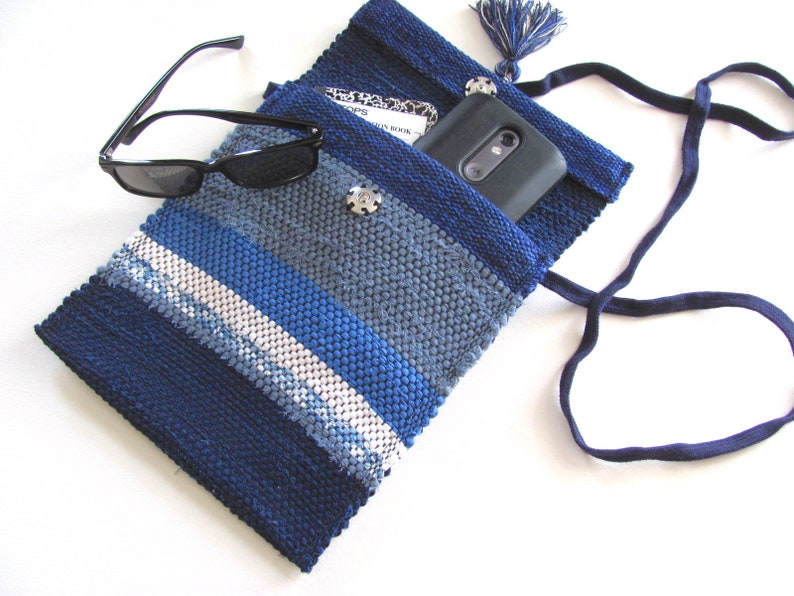 Small Crossbody Bag Wallet or Phone Purse is Handmade, Artisan Hand Woven in Indigo Navy Blue with Zero Waste, Eco Friendly Upcycled Cloth, Vegan Recycled Fabric. This Sustainable Slow Fashion Accessory Handbag, Boho Cash Change Pouch or Money Shoulder Pouch is Handcrafted by Amy C. Lund. Shown open with a phone and notebook inside, black sunglasses on the side.