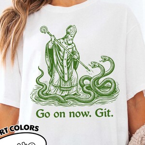 Puede incluir: Una taza de cerámica blanca con asa negra y el texto "But First, Coffee" en negrita negra. La taza se encuentra sobre un fondo borroso, sugiriendo un ambiente acogedor.