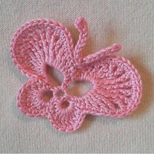 Op de afbeelding: Close-up van een roze gehaakte vlinder. De vlinder heeft gedetailleerde vleugels en antennes. Het haakwerk is zichtbaar en toont de textuur van het garen. De vlinder is een ambachtelijk item.
