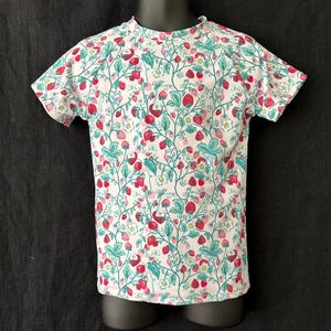 May include: White t-shirt with a red and green strawberry print.