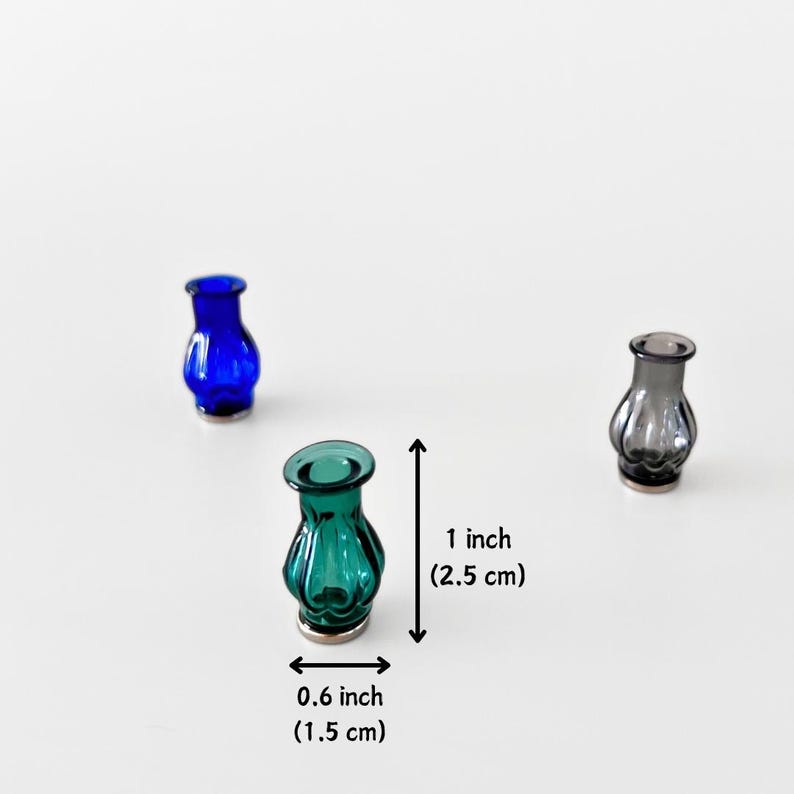 May include: Three small, decorative glass vases in shades of blue, teal, and gray. The teal vase is 1 inch (2.5 cm) tall and 0.6 inches (1.5 cm) wide. The other two vases are similar in size and shape. The vases have a rounded body and a flared top.