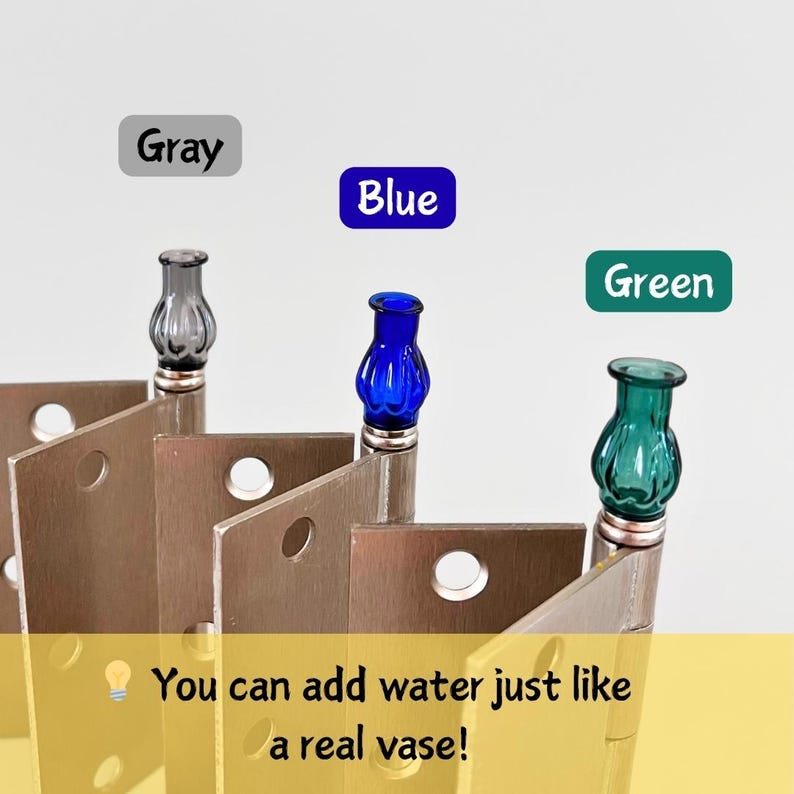 May include: A set of three decorative metal pieces, each topped with a small, colorful glass vase. The vases are gray, blue, and green. The text in the image says, "You can add water just like a real vase!"