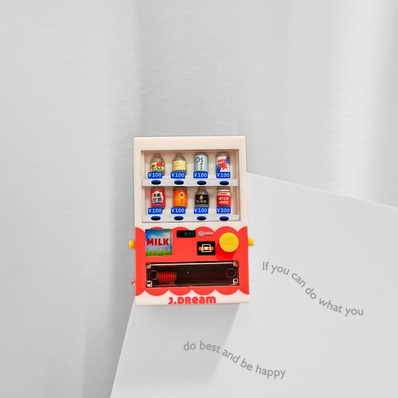 May include: A red and white miniature vending machine with various canned drinks. The machine has a yellow button and the word "MILK" on the front. The text "J.DREAM" is printed on the bottom. The vending machine is a refrigerator magnet.