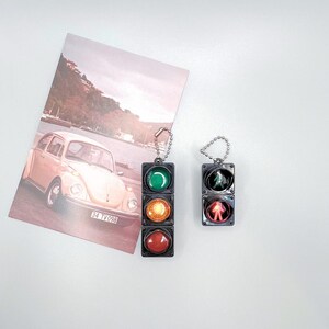 May include: Two black traffic light keychains with red, yellow, and green lights. The keychains are hanging from silver chains.