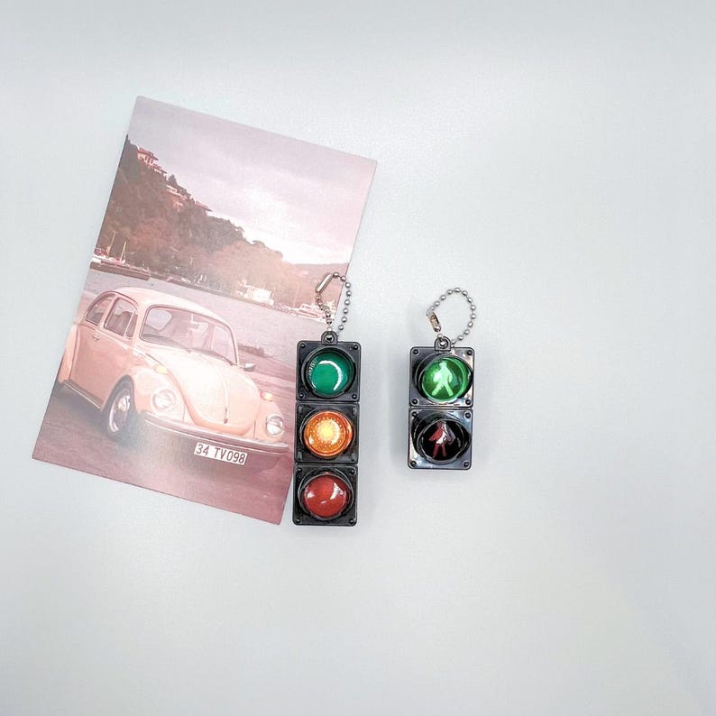May include: Two miniature traffic light keychains. One is green, yellow, and red. The other is green, yellow, and red with a pedestrian symbol.