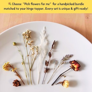 May include: A selection of dried flowers in various colors, including yellow, white, and brown, arranged on a white plate. The image includes text that reads, "Choose 'Pick flowers for me' for a handpicked bundle matched to your hinge topper."