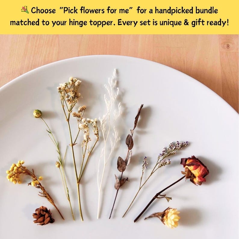 May include: A selection of dried flowers in various colors, including yellow, white, and brown, arranged on a white plate. The image includes text that reads, "Choose 'Pick flowers for me' for a handpicked bundle matched to your hinge topper."