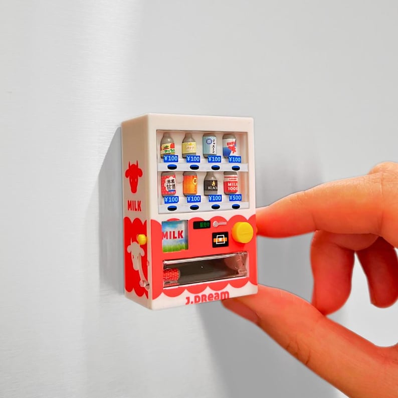 May include: Miniature white and red vending machine with various beverage cans and bottles. The machine has a yellow button and the word "MILK" on the front. The text "1.dream" is at the bottom.
