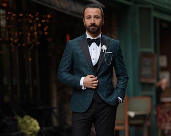 Può includere: Una giacca da smoking verde acqua fantasia con revers neri, indossata sopra un gilet e pantaloni neri. L'ensemble include una camicia bianca, un papillon nero e un fiore bianco all'occhiello. Una catena dell'orologio da tasca aggiunge un tocco classico.