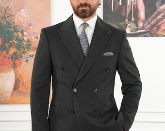 Puede incluir: Un traje cruzado gris oscuro con camisa blanca y corbata estampada. El traje tiene solapas de muesca, varios botones y un pañuelo de bolsillo. El hombre está de pie frente a una pintura.