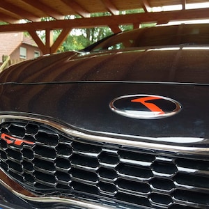 Peut inclure: Une voiture noire avec un emblème "GT" rouge et noir sur la calandre avant. La voiture a un emblème noir et rouge sur le capot.