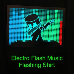 May include: Black shirt featuring a neon graphic of a DJ in a marshmallow helmet, dabbing in front of a sound equalizer. The text "Electro Flash Music Flashing Shirt" is displayed in green below the graphic.