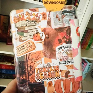 May include: A clear case for an e-reader, decorated with autumn-themed stickers. The design includes stacks of books, pumpkins, and the text "hello PUMPKIN SEASON". The case is held in a person's hand, with a bookshelf in the background.