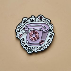 Peut inclure: Épingle en émail lavande représentant un téléphone vintage avec un cadran en forme de cœur. L'épingle porte l'inscription "CALL ME ANTISOCIAL BUT PLEASE DON'T CALL ME" en blanc, avec des lèvres rouges et des feuilles vertes.