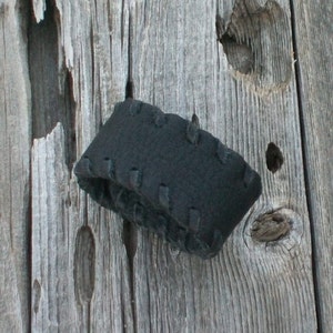 May include: A black fabric headband with a stitched design, hanging on a weathered wooden surface.