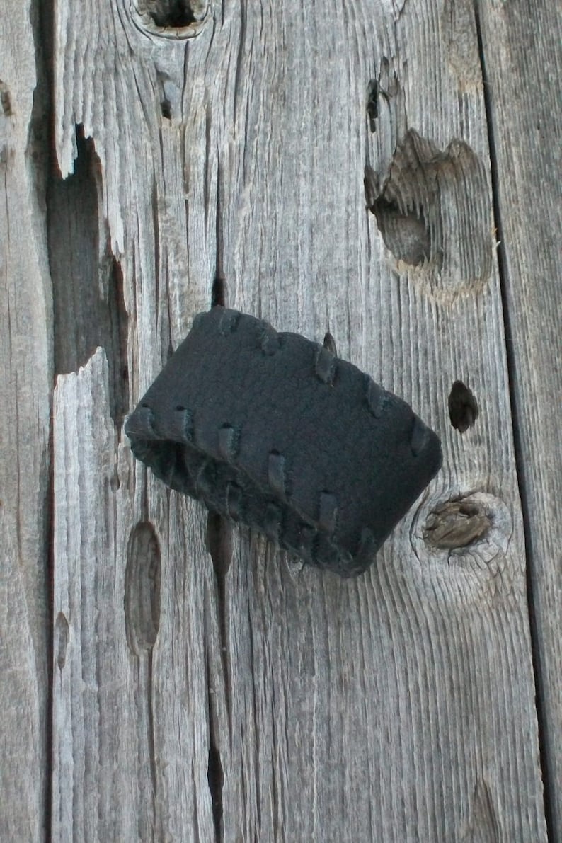 May include: A black fabric headband with a stitched design, hanging on a weathered wooden surface.