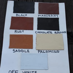 K&ouml;nnte beinhalten: Eine wei&szlig;e Karte mit Lederproben in verschiedenen Farben, darunter Schwarz, Mahagoni, Rost, Schokoladenbraun, Sattel, Palomino und Off-White. Die Farben sind unter jeder Probe beschriftet.