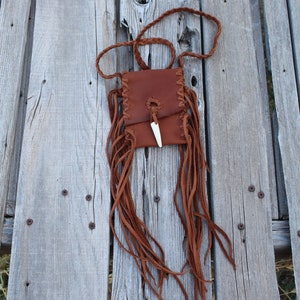 Pu&ograve; includere: Una borsa in pelle marrone con frange e un accento in osso. La borsa &egrave; appesa a una tracolla in pelle intrecciata.
