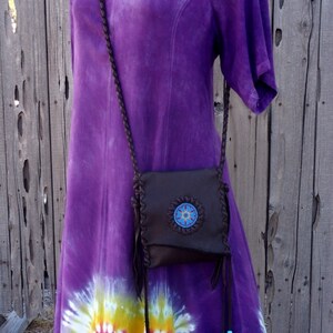 May include: A brown leather crossbody bag with a beaded design and fringe accents. The bag is worn over a purple tie-dye dress.