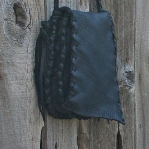K&ouml;nnte beinhalten: Eine schwarze Leder-Umh&auml;ngetasche mit geflochtenem Riemen. Die Tasche hat einen Klappverschluss und ist aus weichem, geschmeidigem Leder gefertigt.