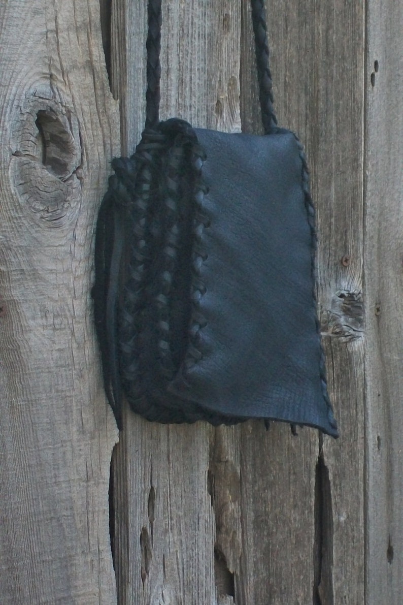 K&ouml;nnte beinhalten: Eine schwarze Leder-Umh&auml;ngetasche mit geflochtenem Riemen. Die Tasche hat einen Klappverschluss und ist aus weichem, geschmeidigem Leder gefertigt.