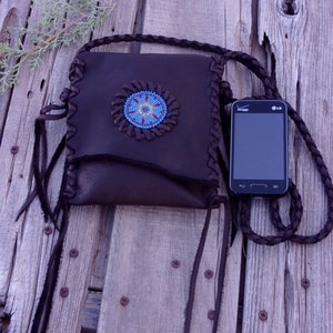 May include: A brown leather purse with a beaded design and fringe. The purse has a long strap and is decorated with turquoise beads. A black cell phone with the LG logo is visible in the image.
