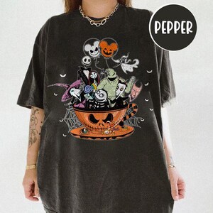 May include: Black t-shirt featuring a Halloween-themed graphic. The design includes characters from "The Nightmare Before Christmas" inside a jack-o'-lantern teacup. The word "Pepper" is printed on a black circle.