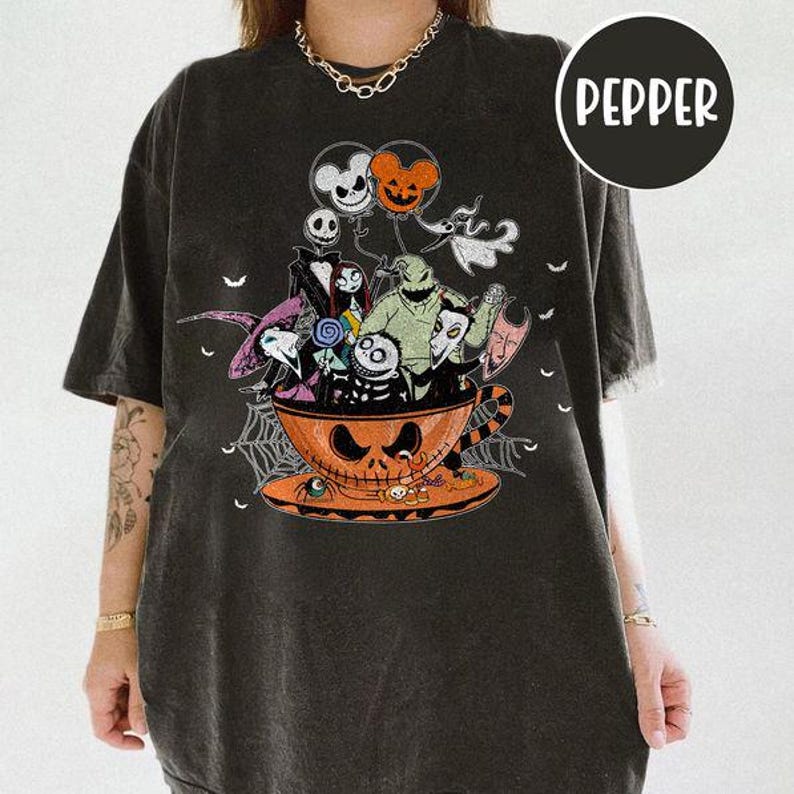 May include: Black t-shirt featuring a Halloween-themed graphic. The design includes characters from "The Nightmare Before Christmas" inside a jack-o'-lantern teacup. The word "Pepper" is printed on a black circle.
