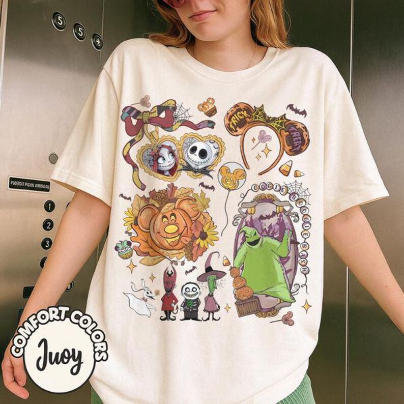 Pode incluir: Uma t-shirt de manga curta cor de creme com uma impress&atilde;o gr&aacute;fica de personagens e &iacute;cones de O Estranho Mundo de Jack, incluindo Jack Skellington, Sally, Oogie Boogie, Zero e v&aacute;rios motivos sazonais como ab&oacute;boras e orelhas.