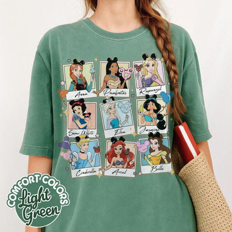 May include: Light green Comfort Colors t-shirt featuring nine Disney princess portraits with mouse ears and names. The shirt has a round neckline and short sleeves. The text "Comfort Colors Light Green" is on the bottom left.